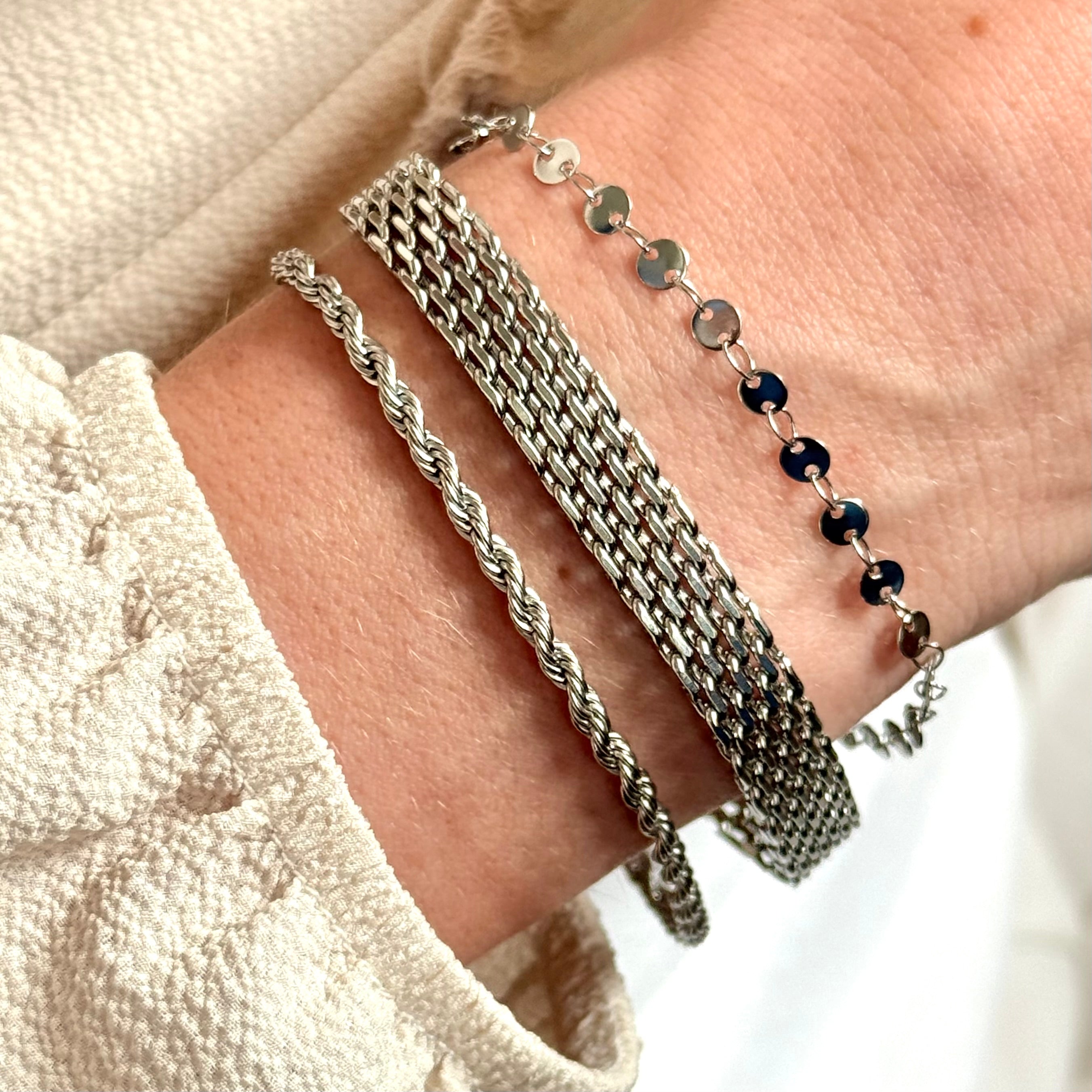 Close-up of a wrist wearing multiple silver bracelets on a neutral background