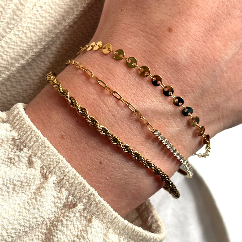 Close-up of a wrist wearing multiple gold bracelets on a neutral background