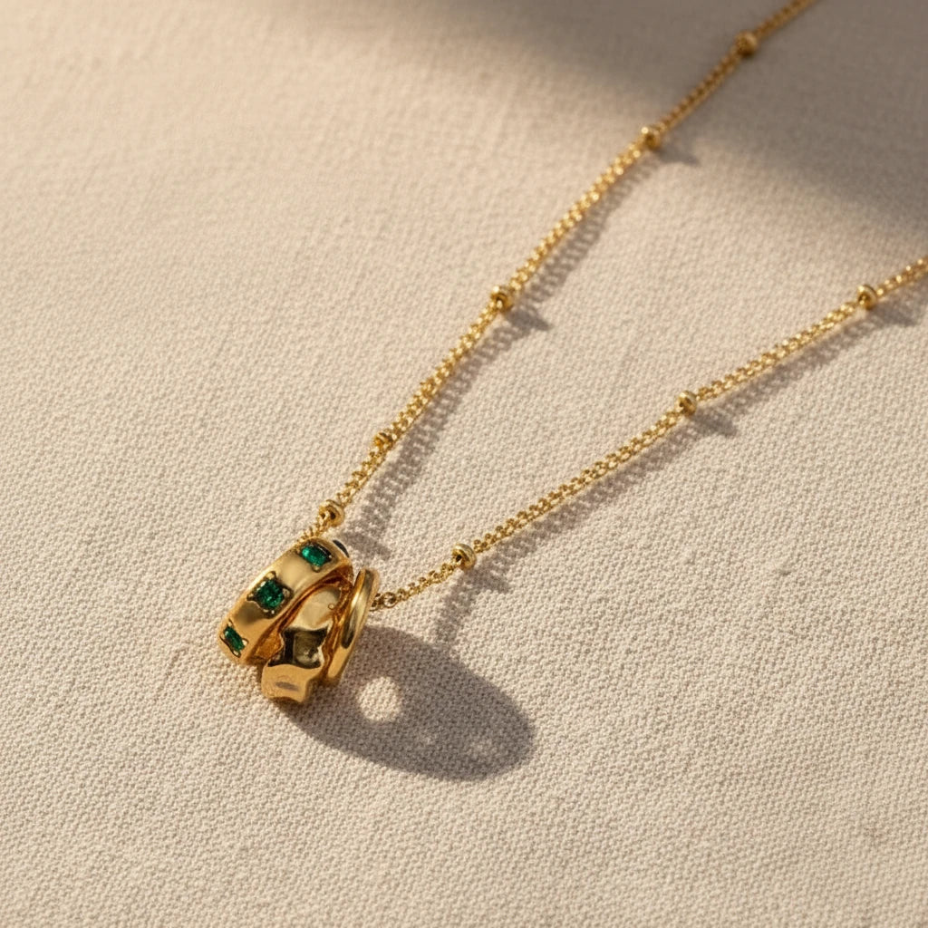 Gold necklace with a unique pendant with three circles and emerald stone on a white background. Emerald pendant necklace gold, three circle necklace, green stone necklace