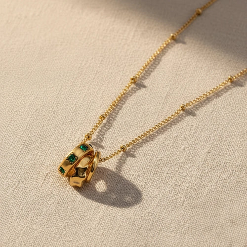 Gold necklace with a unique pendant with three circles and emerald stone on a white background. Emerald pendant necklace gold, three circle necklace, green stone necklace