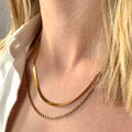 Close-up of a person wearing two gold necklaces herringbone and snake on a woman's neck. Simple gold chains, stainless steel jewelry