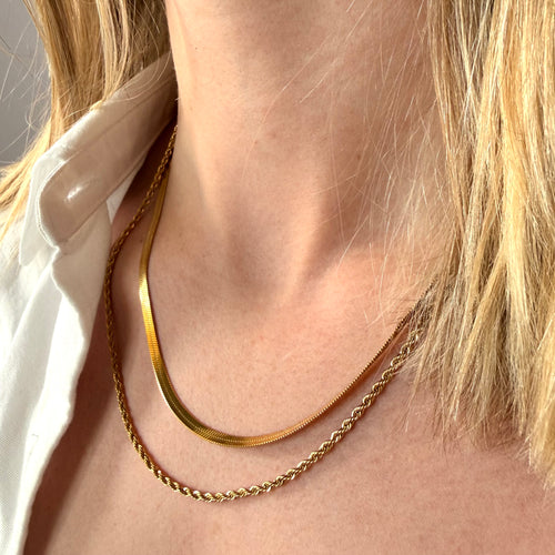 Close-up of a person wearing two gold necklaces herringbone and snake on a woman's neck. Simple gold chains, stainless steel jewelry