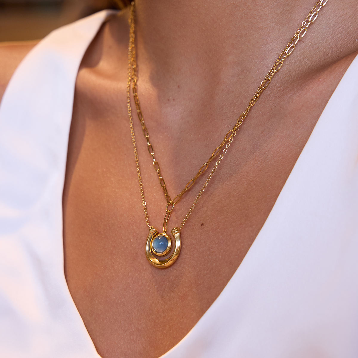 Gold necklace with a blue pendant on a person wearing a white top.