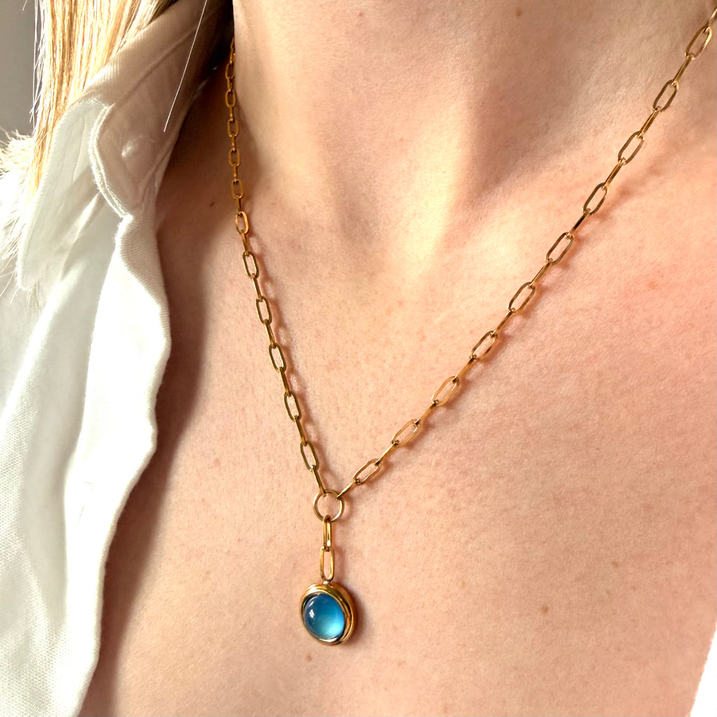 Gold necklace with a blue pendant worn by a person