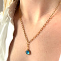 Gold necklace with a blue pendant worn by a person