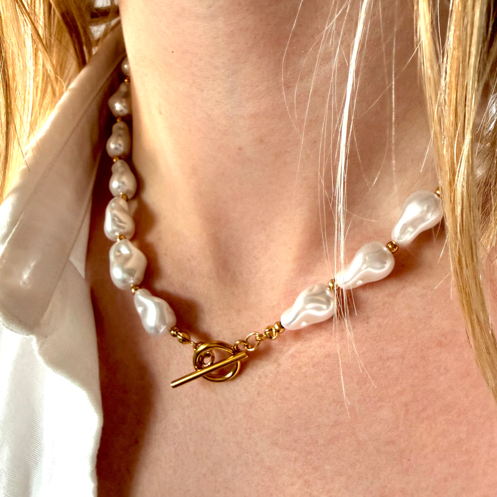 Pearl necklace with a gold clasp worn by a person with blonde hair. Chunky pearl necklace. 