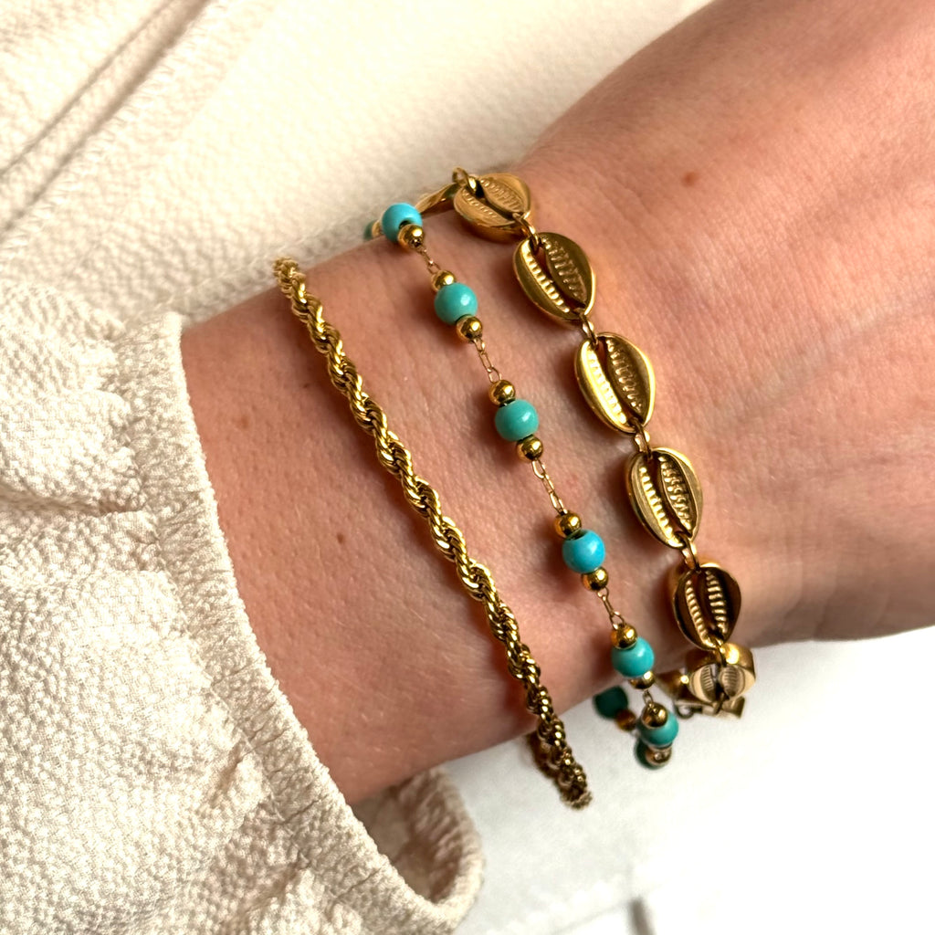 Stack of three gold bracelts and turquoise beaded bracelet on a wrist against a neutral background. rope chain bracelet gold, gold chain bracelet, textured bracelet