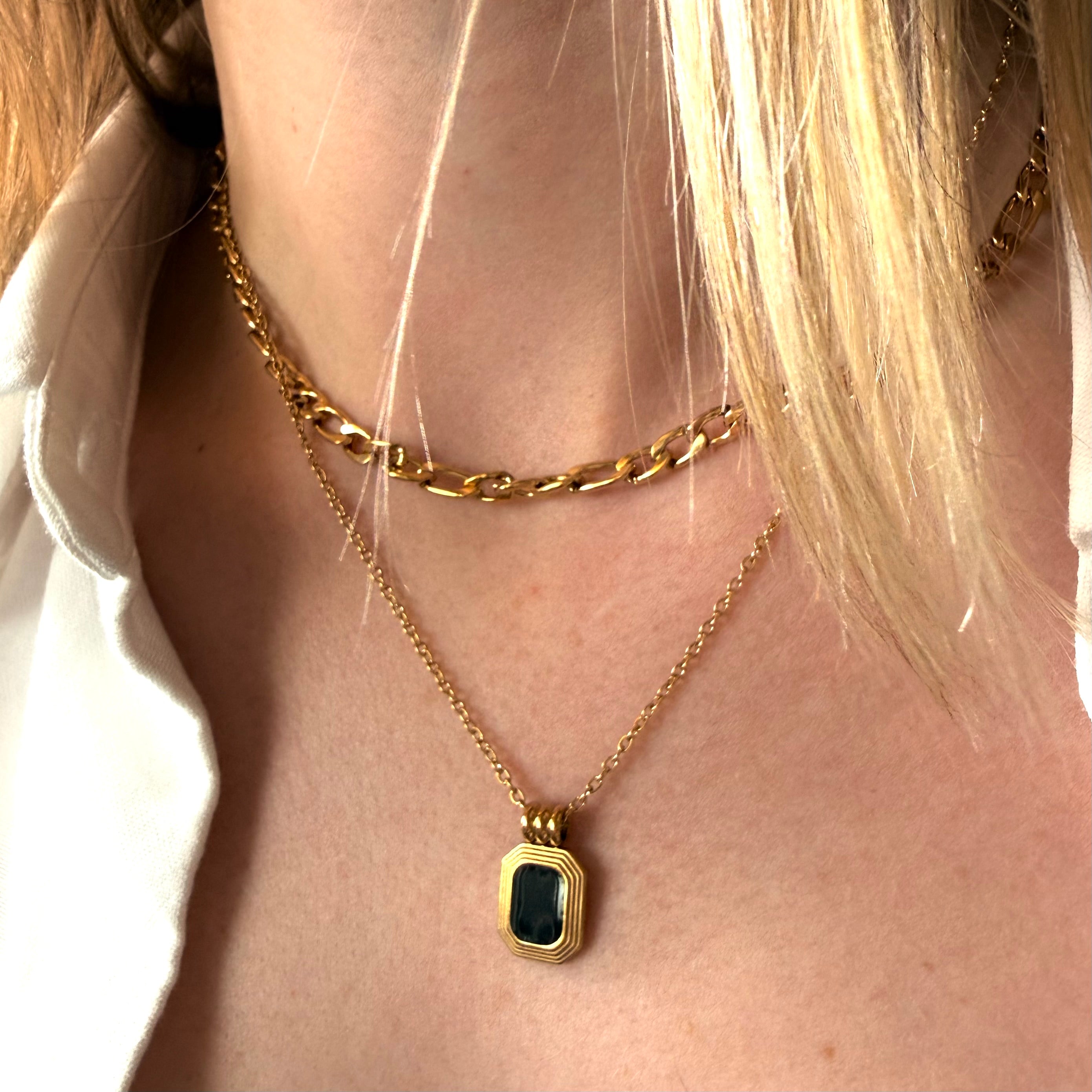 Close-up of a person wearing a gold necklace with a black and gold emerald shaped pendant.