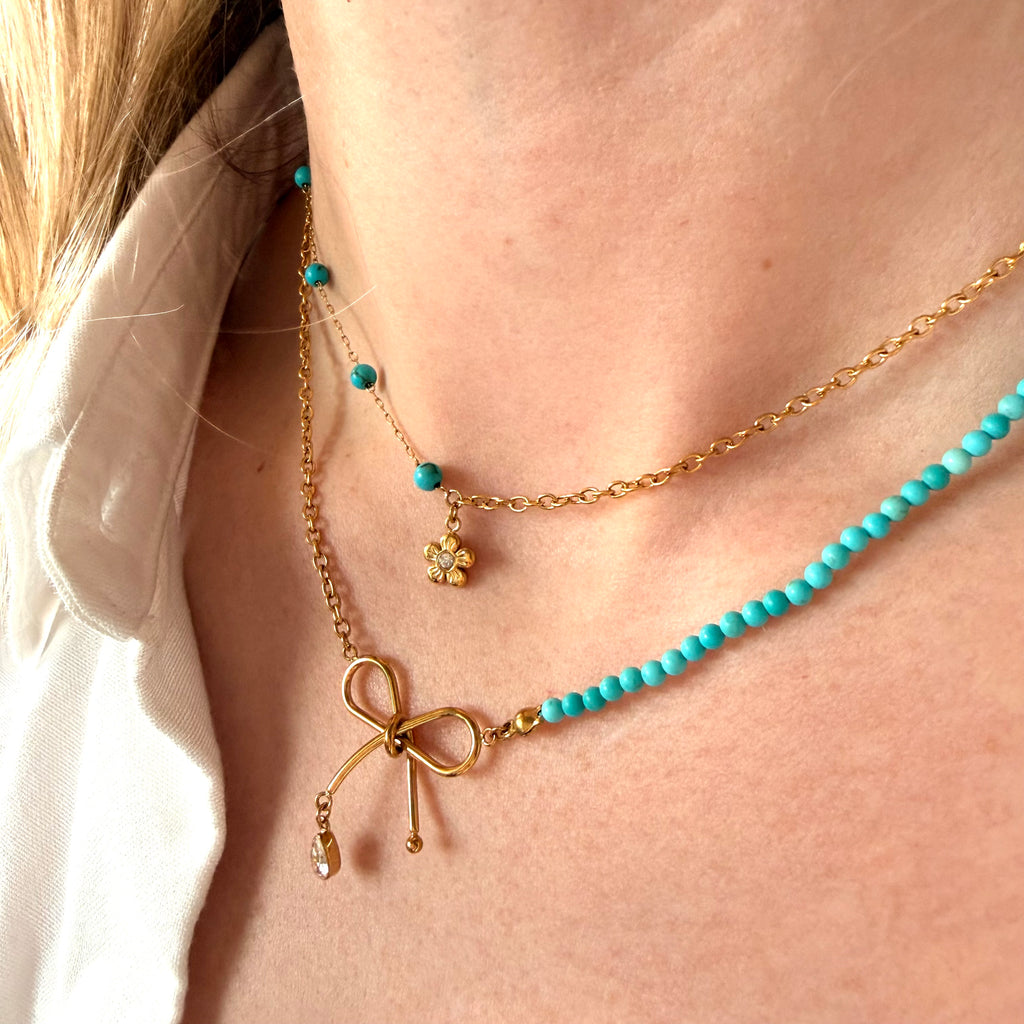 Close-up of a person wearing a gold and turquoise beaded necklace with a bow and flower design.