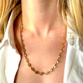 Gold coffee bean chain necklace worn by a person with a white shirt