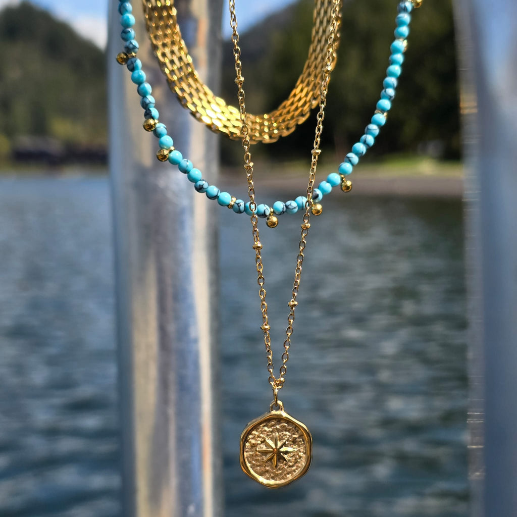 Three necklaces with turquoise beads and gold chains against a blurred natural water background. 