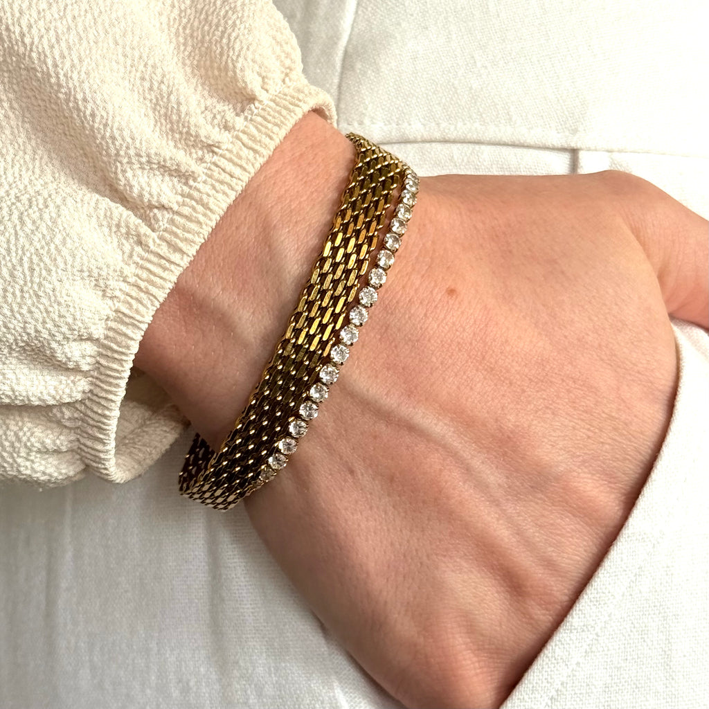 Gold bracelets with small zirconia stones and mesh bracelet on a wrist against a white background. Gold bracelet stack, luxury bracelet stack