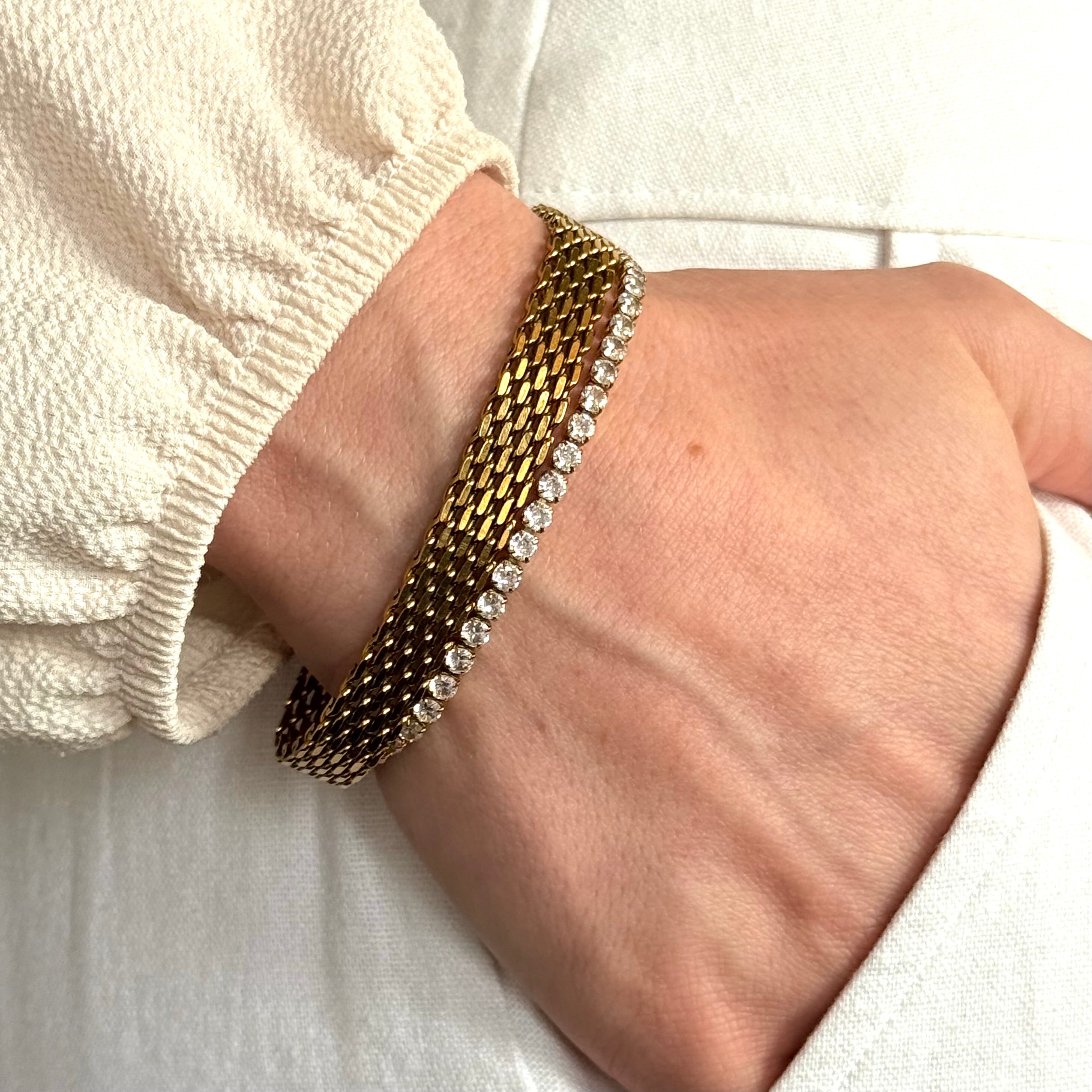 Gold bracelets with small zirconia stones and mesh bracelet on a wrist against a white background. Gold bracelet stack, luxury bracelet stack