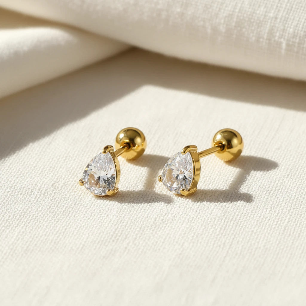 Gold stud earrings with teardrop zirconia gemstones on a white surface. teardrop zirconia stud earrings, gold stud earrings, dainty gold earrings