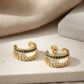Gold hoop earrings with green emerald gemstones on a white surface