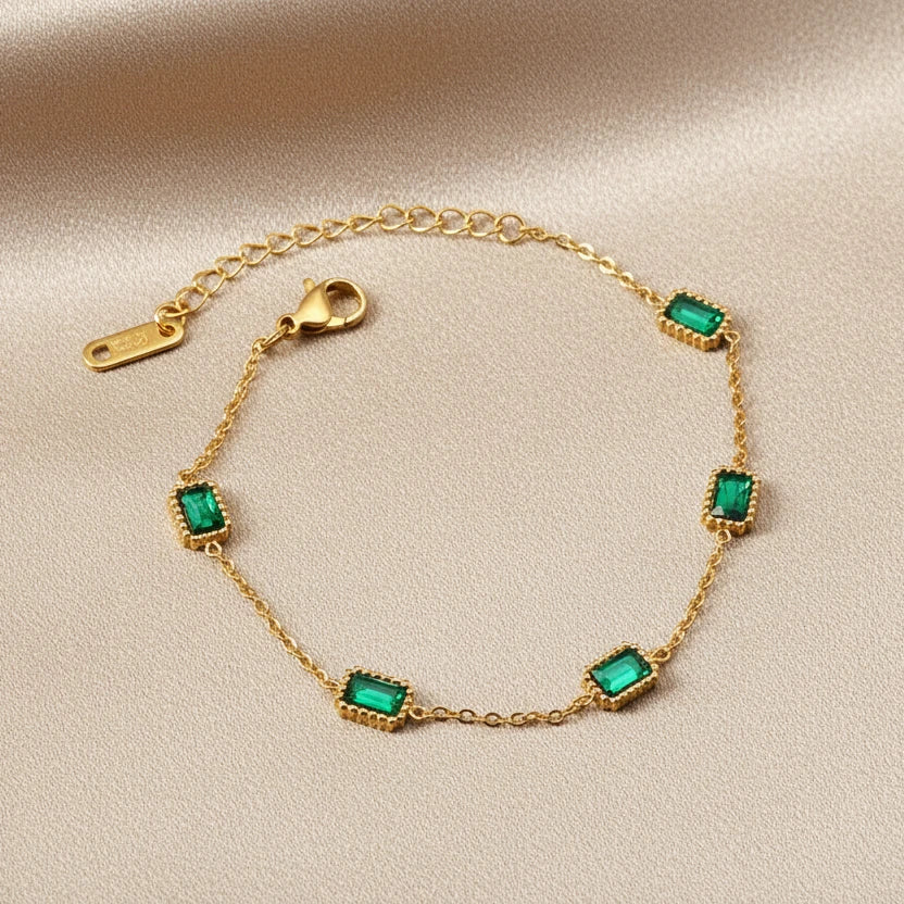 Gold bracelet with green/emerald gemstones on a white surface