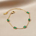 Gold bracelet with green/emerald gemstones on a white surface