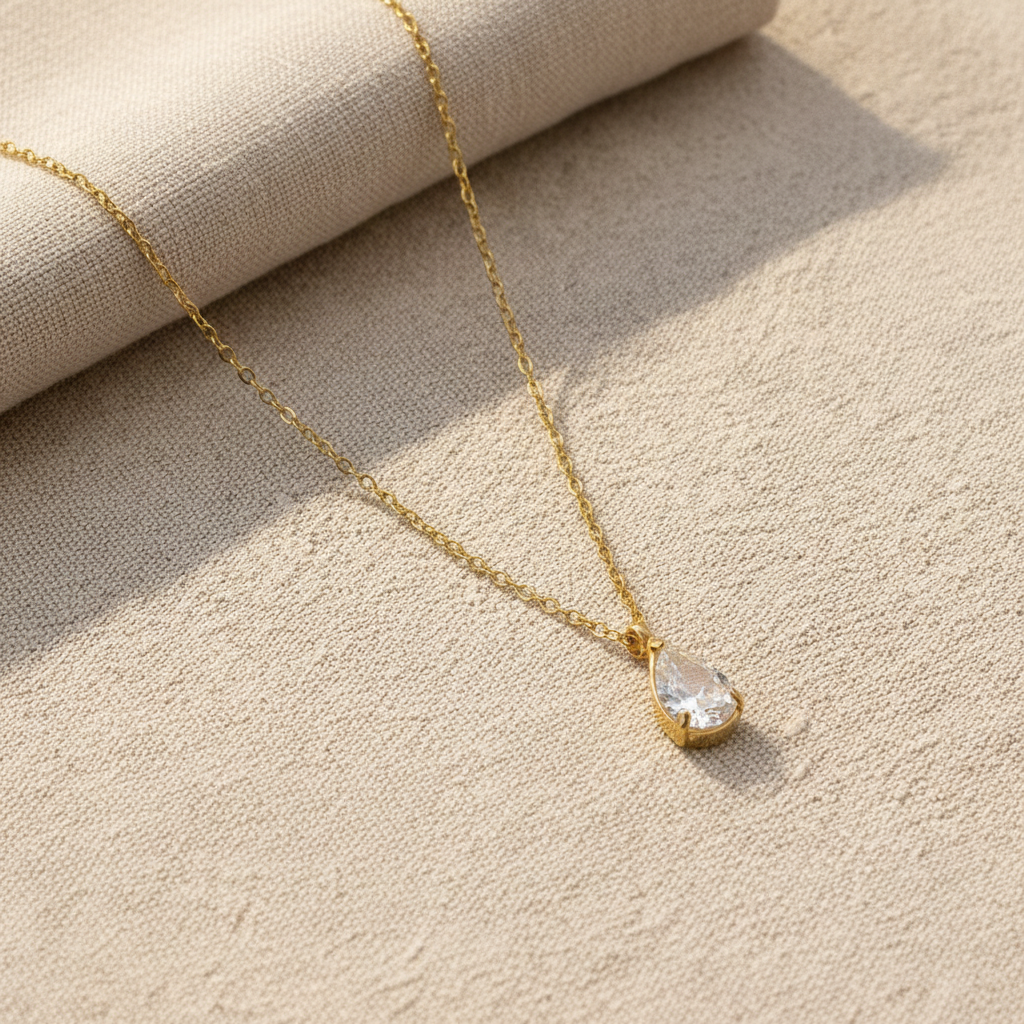 Gold necklace with a zirconia pendant on a textured white surface. teardrop zirconia necklace gold, crystal pendant necklace, dainty gold necklace