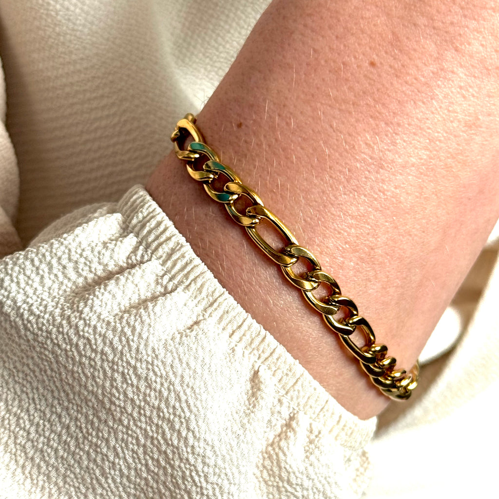 Gold Figaro chain bracelet on a wrist with a neutral background. Classic chain bracelet