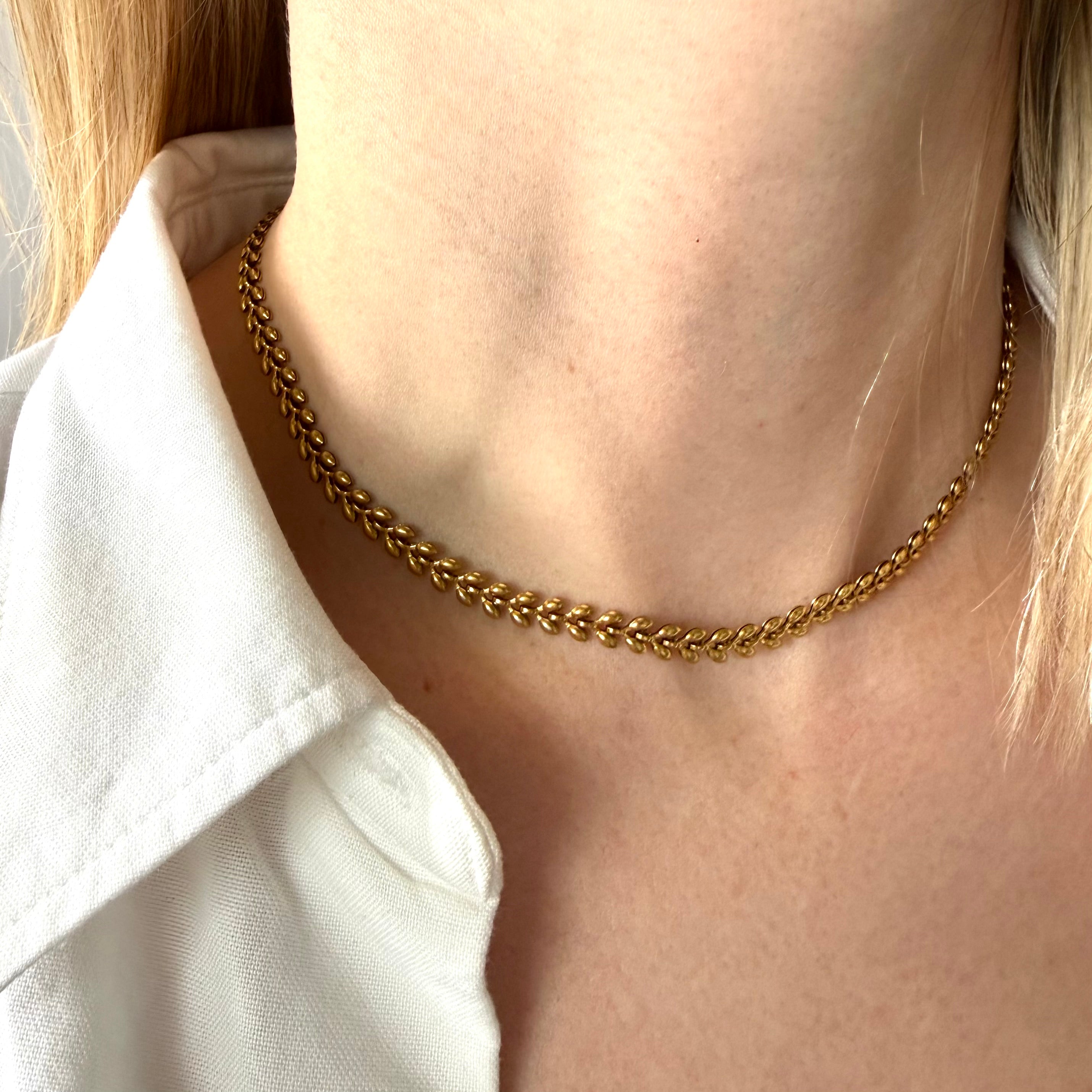 Gold fishbone chain necklace worn by a person with a white shirt