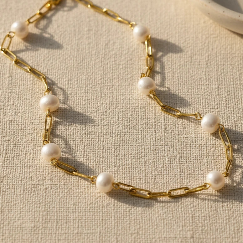Gold chain necklace with pearls on a textured white surface
