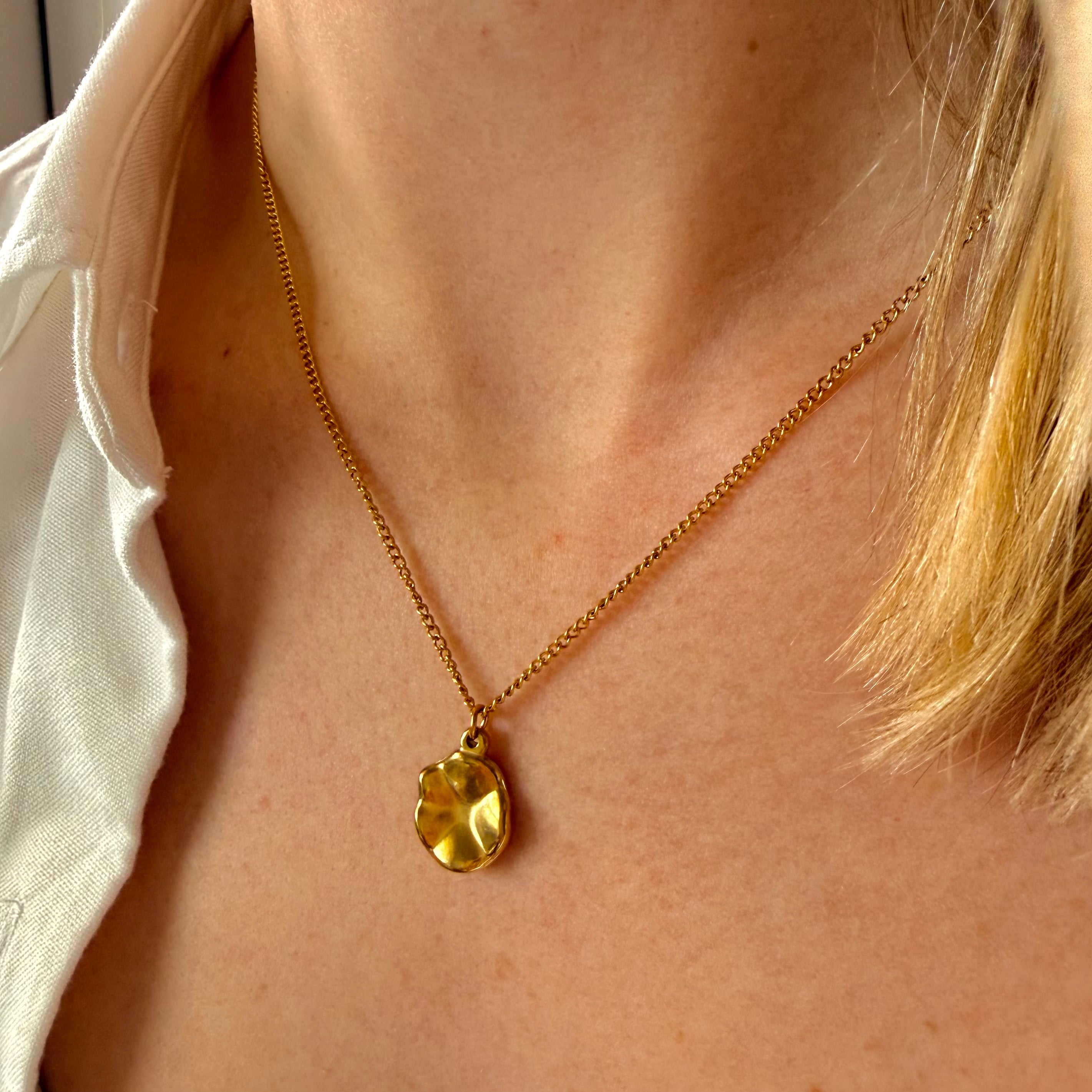 Gold necklace with a gold geometric pendant worn by a person. oval pendant necklace gold, geometric gold necklace, minimalist pendant necklace
