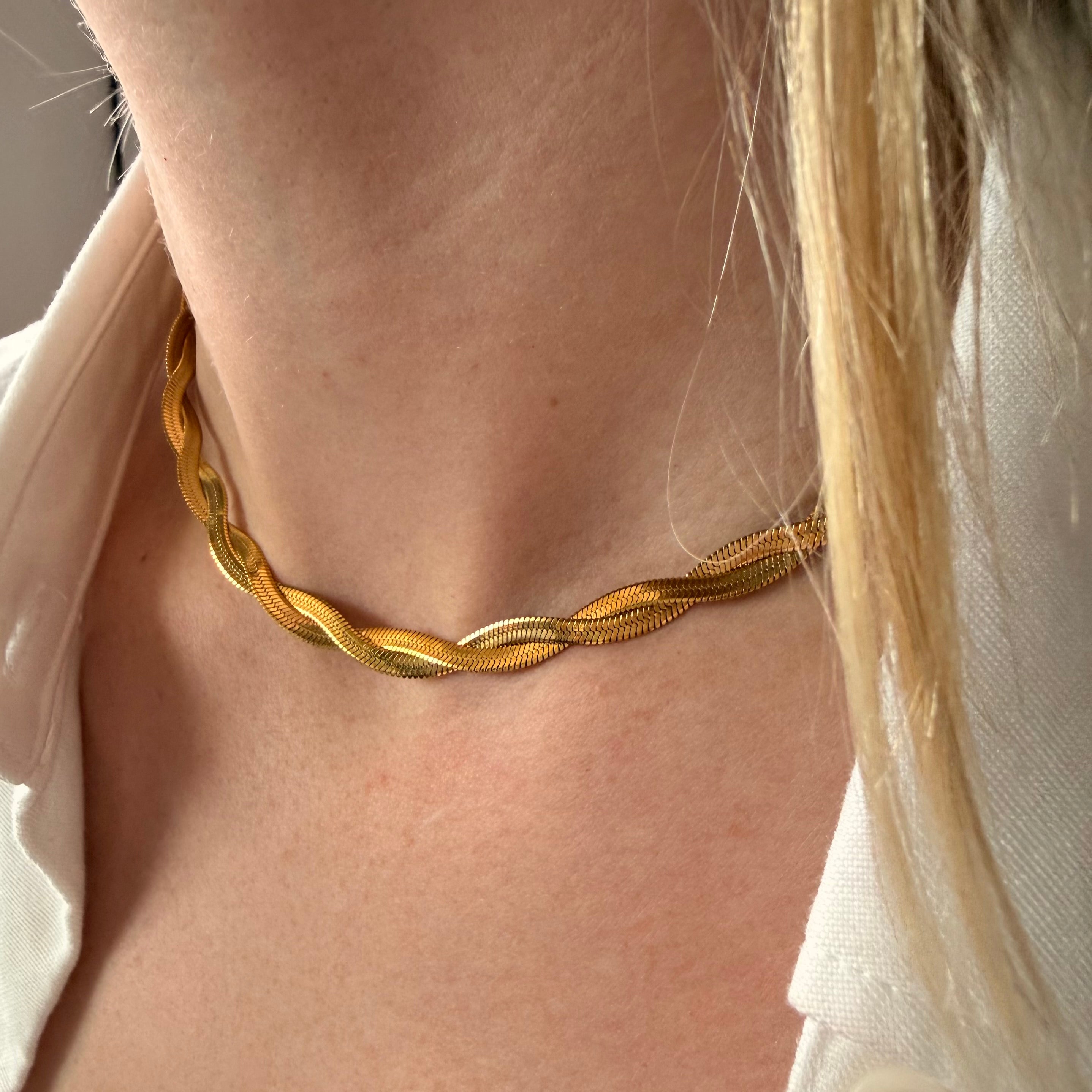 Close-up of a person wearing a gold braided necklace with a neutral background. twisted herringbone necklace gold, flat chain necklace, gold chain necklace