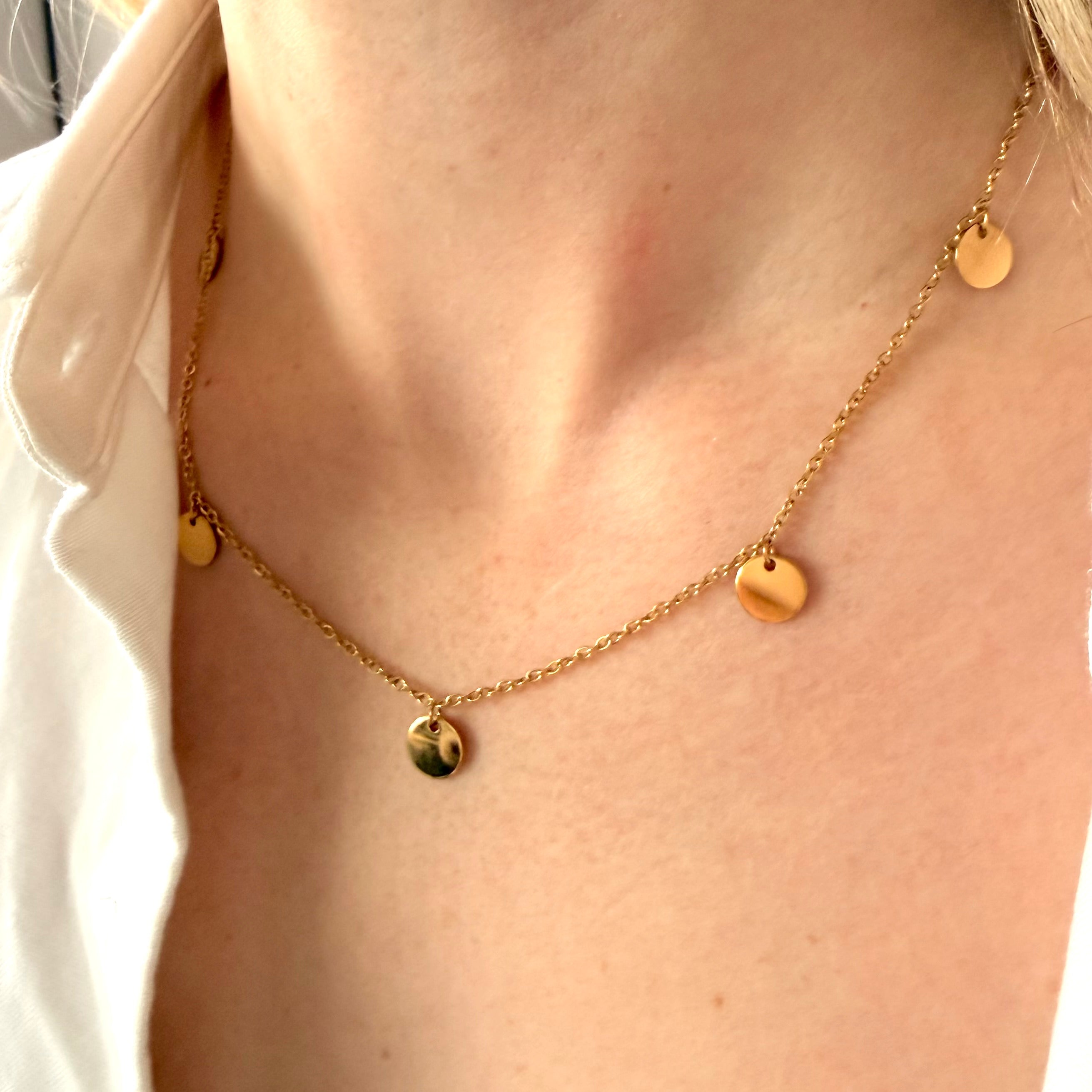 Gold necklace with small round pendants on a person wearing a white shirt.