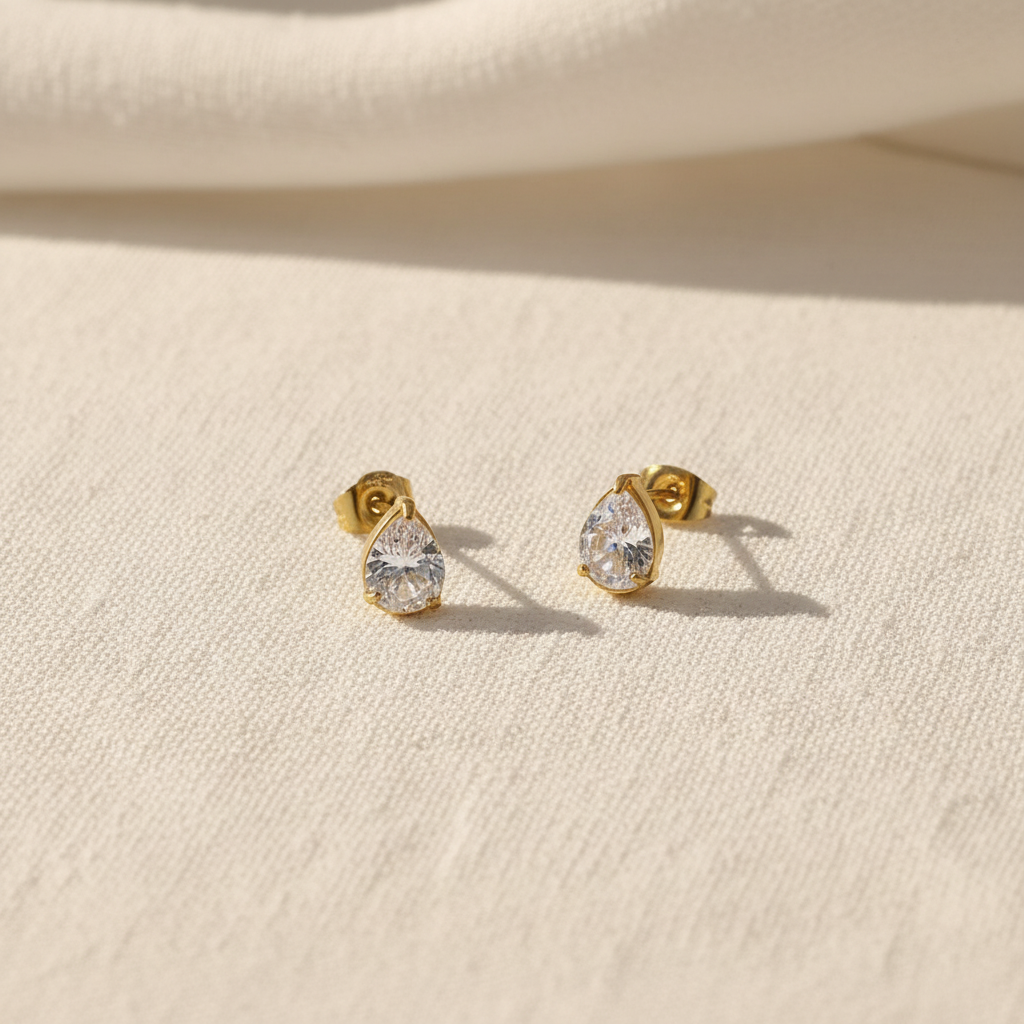 Gold stud earrings with zirconia gemstones on a white textured surface