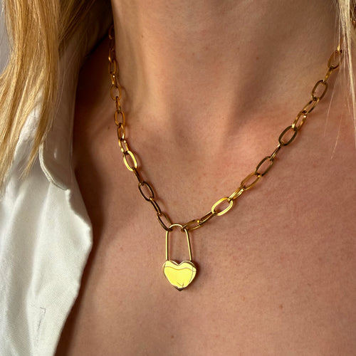 Gold chain necklace with a heart-shaped lock pendant on a person wearing a white shirt.