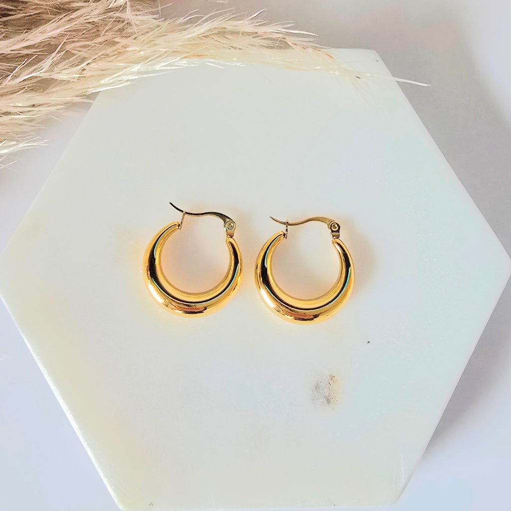 Gold hoop earrings on a white marblebackground