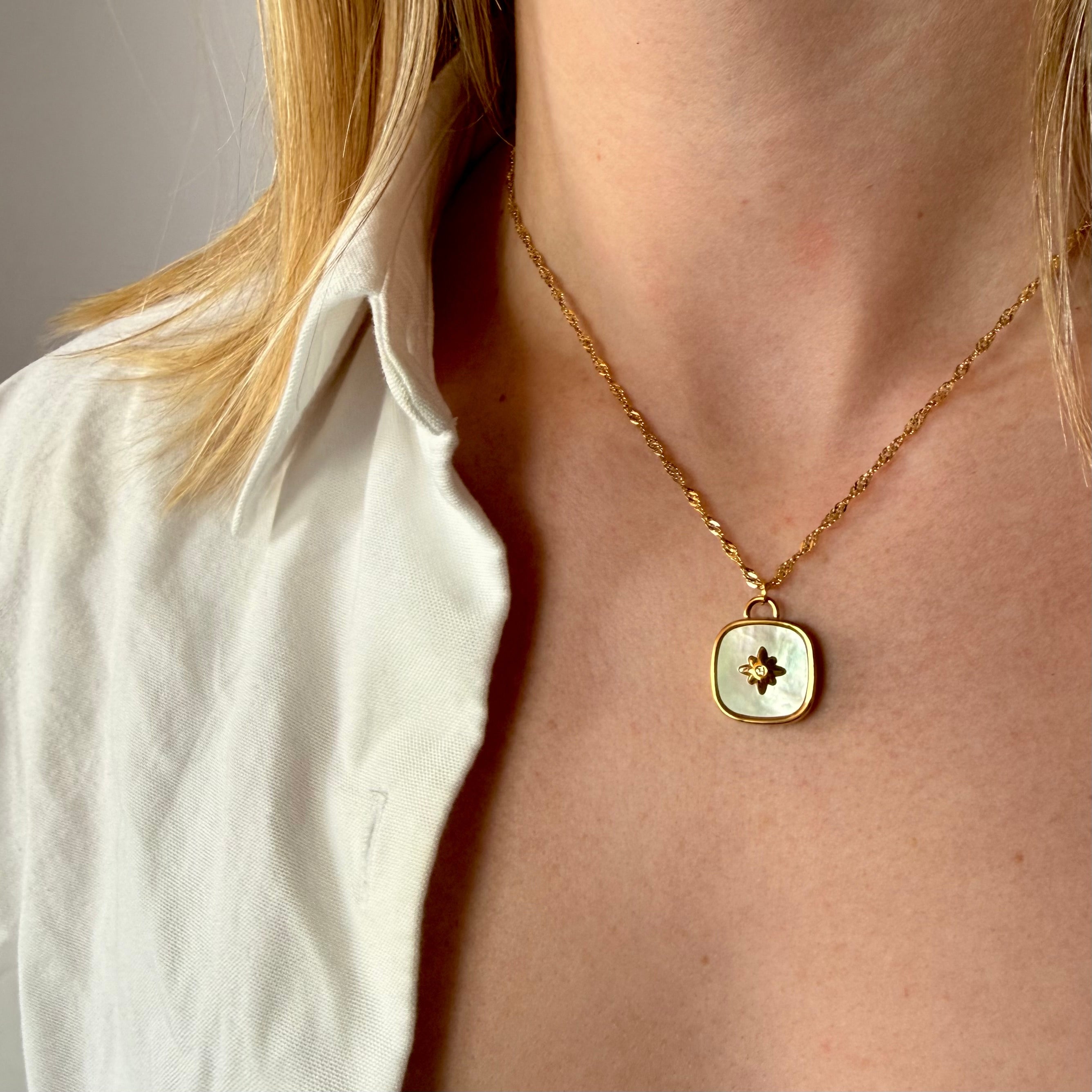 Gold necklace with a square pendant worn by a person against a neutral background