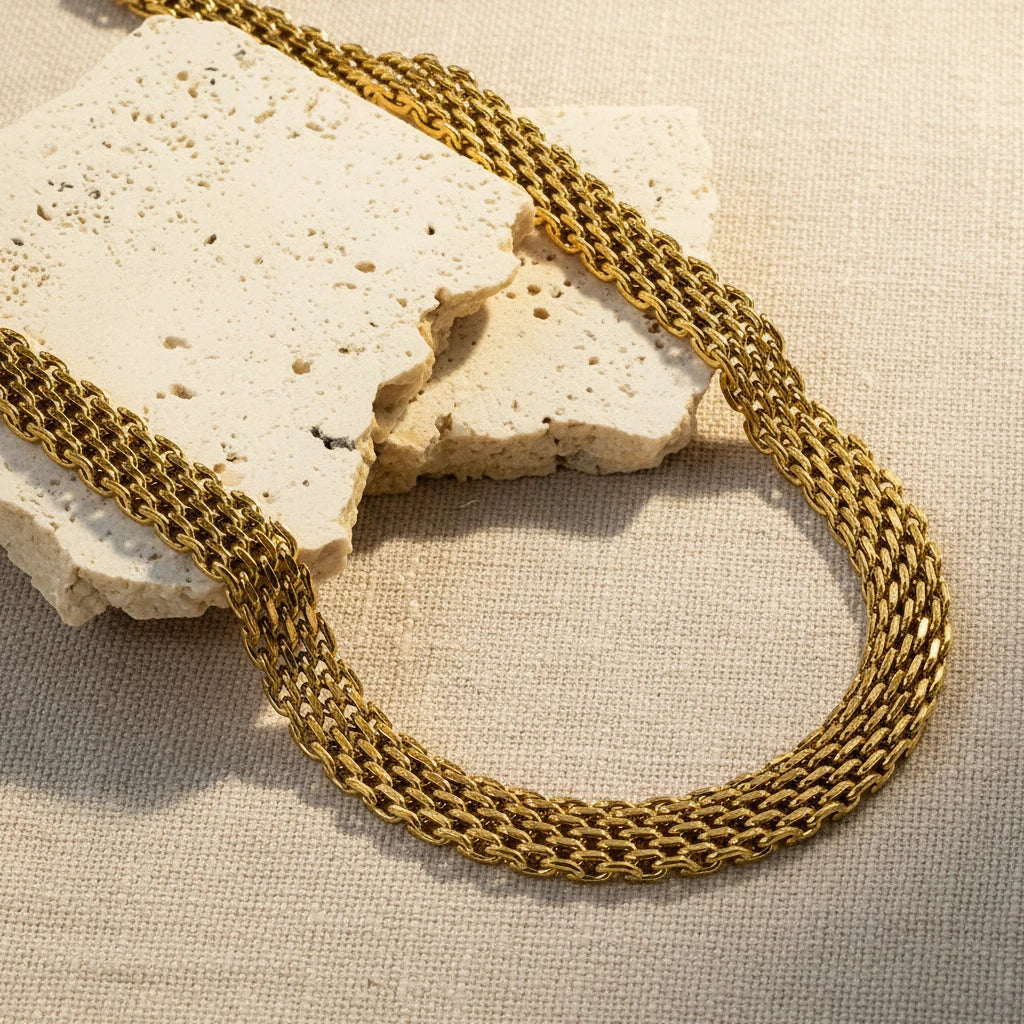 Gold mesh chain on a textured white surface. gold mesh choker necklace, woven chain choker, flat gold choker