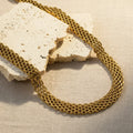 Gold mesh chain on a textured white surface. gold mesh choker necklace, woven chain choker, flat gold choker