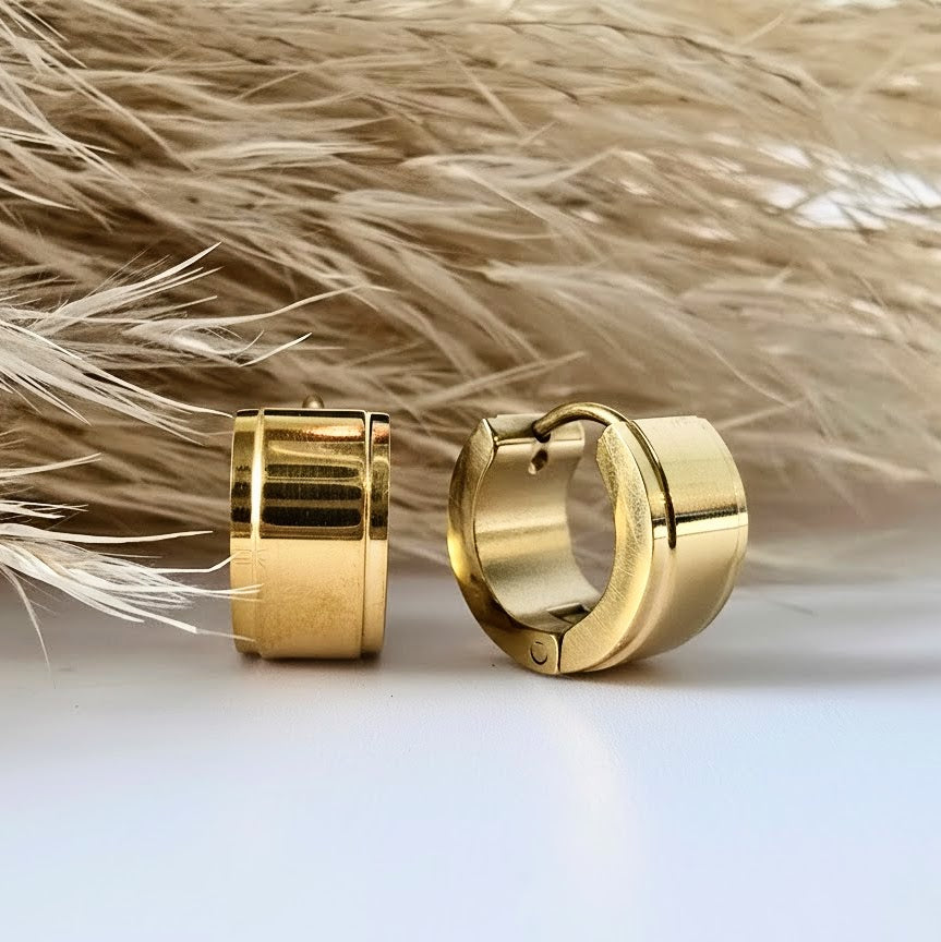 Gold huggie earrings on a light background with dried grass.