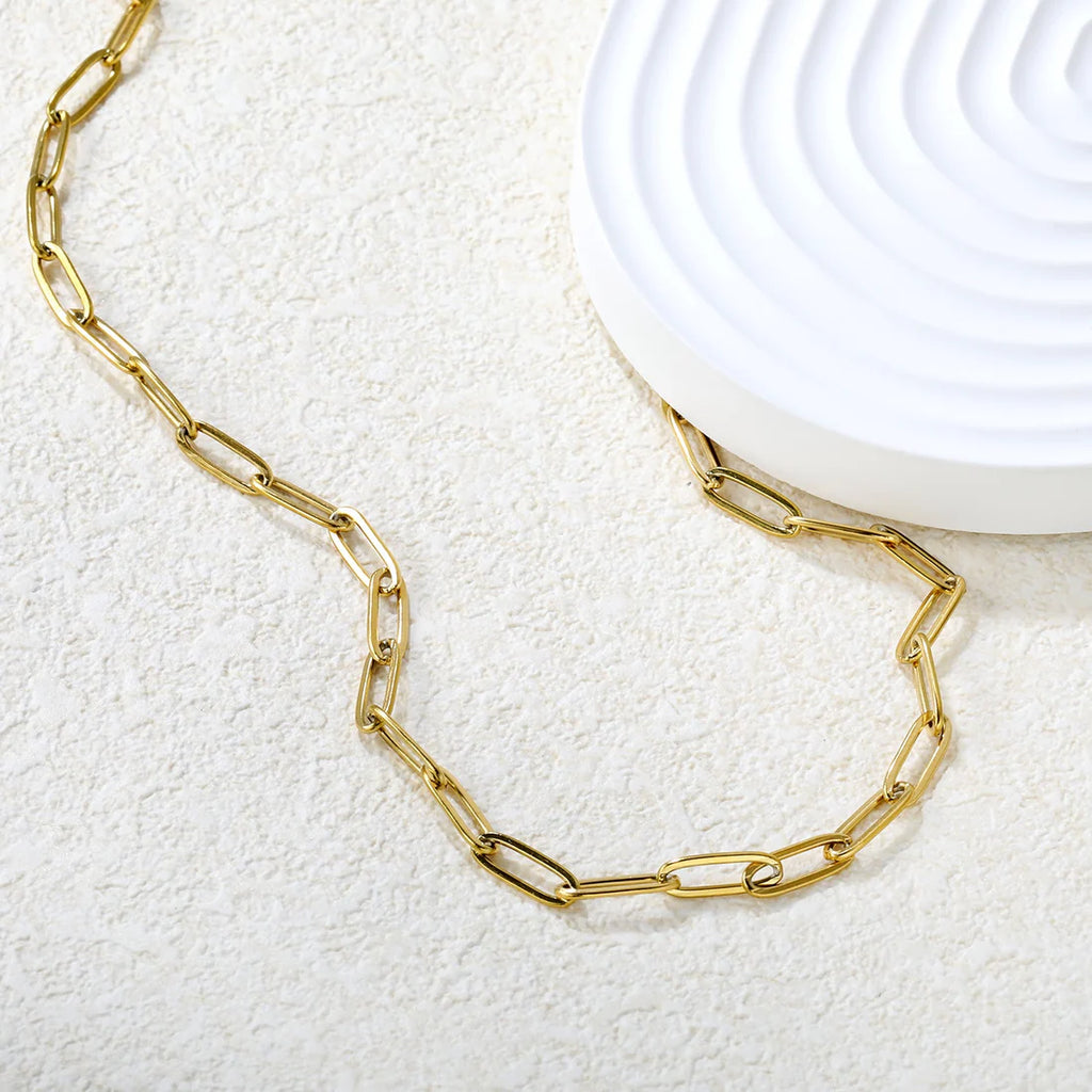 Gold chain paperclip necklace on a textured white surface with a white ceramic dish in the background.