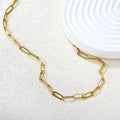 Gold chain paperclip necklace on a textured white surface with a white ceramic dish in the background.