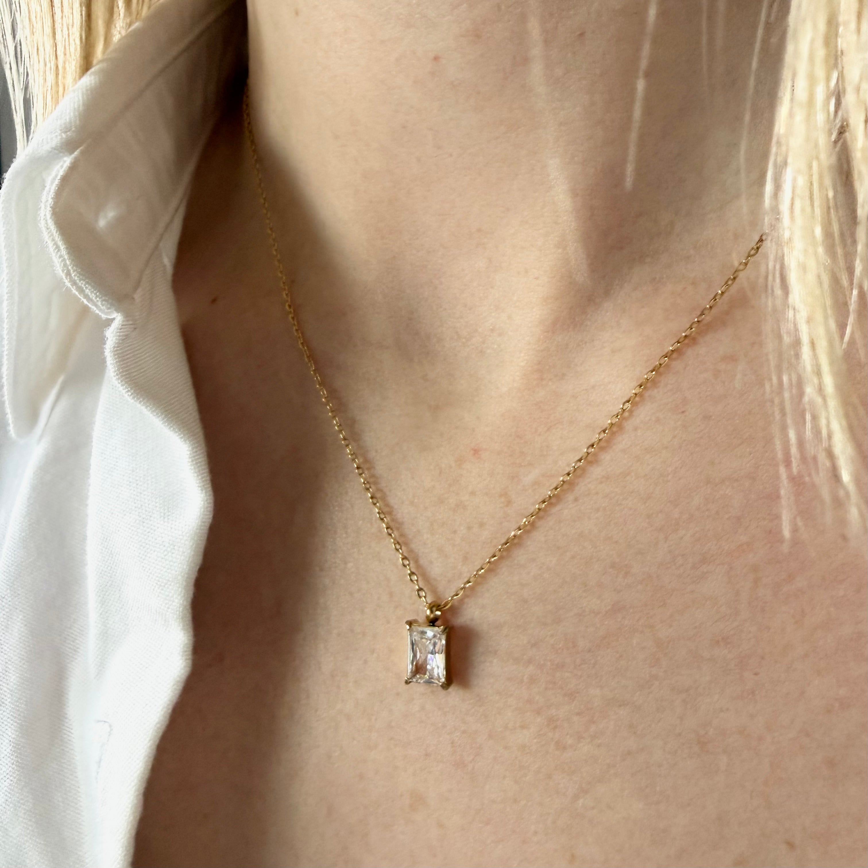 Gold necklace with a zirconia diamond pendant worn by a woman in a white shirt. rectangular zirconia necklace gold, crystal pendant necklace, minimalist gold necklace