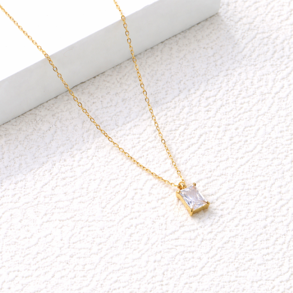 Gold necklace with a rectangular pendant on a textured white surface. rectangular zirconia necklace gold, crystal pendant necklace, minimalist gold necklace