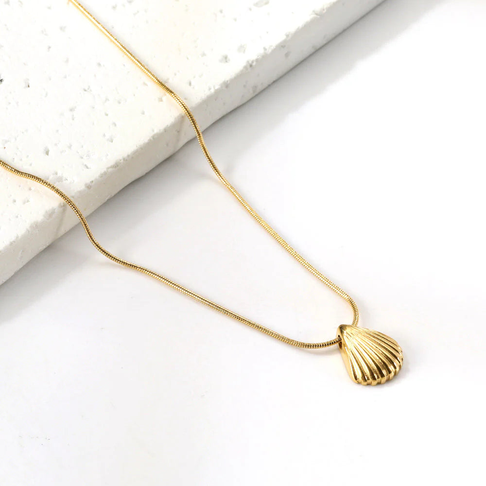 Gold necklace with a shell pendant on a white surface. Beach necklace. Ocean inspired jewelry