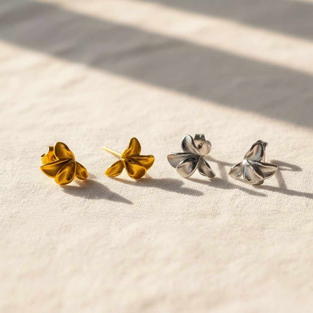 Gold and silver flower earrings on a white surface with dried grass.