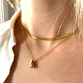 Close-up of a person wearing a gold necklace with a small teardrop pendant. teardrop pendant necklace gold, minimalist drop necklace, dainty gold necklace