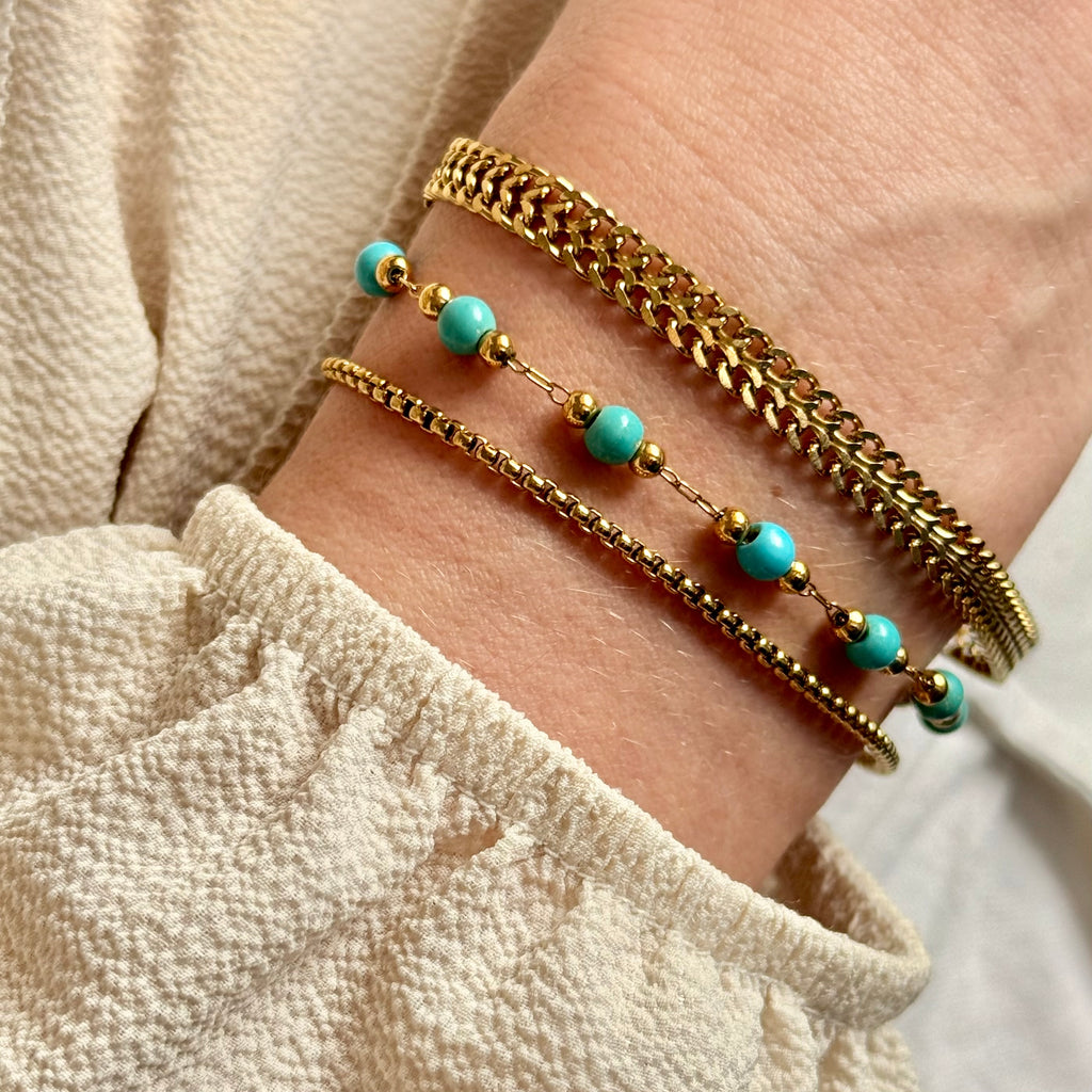 Close-up of a wrist wearing two gold bracelets with turquoise beads on a neutral background. braided gold bracelet, rope chain bracelet, dainty gold bracelet