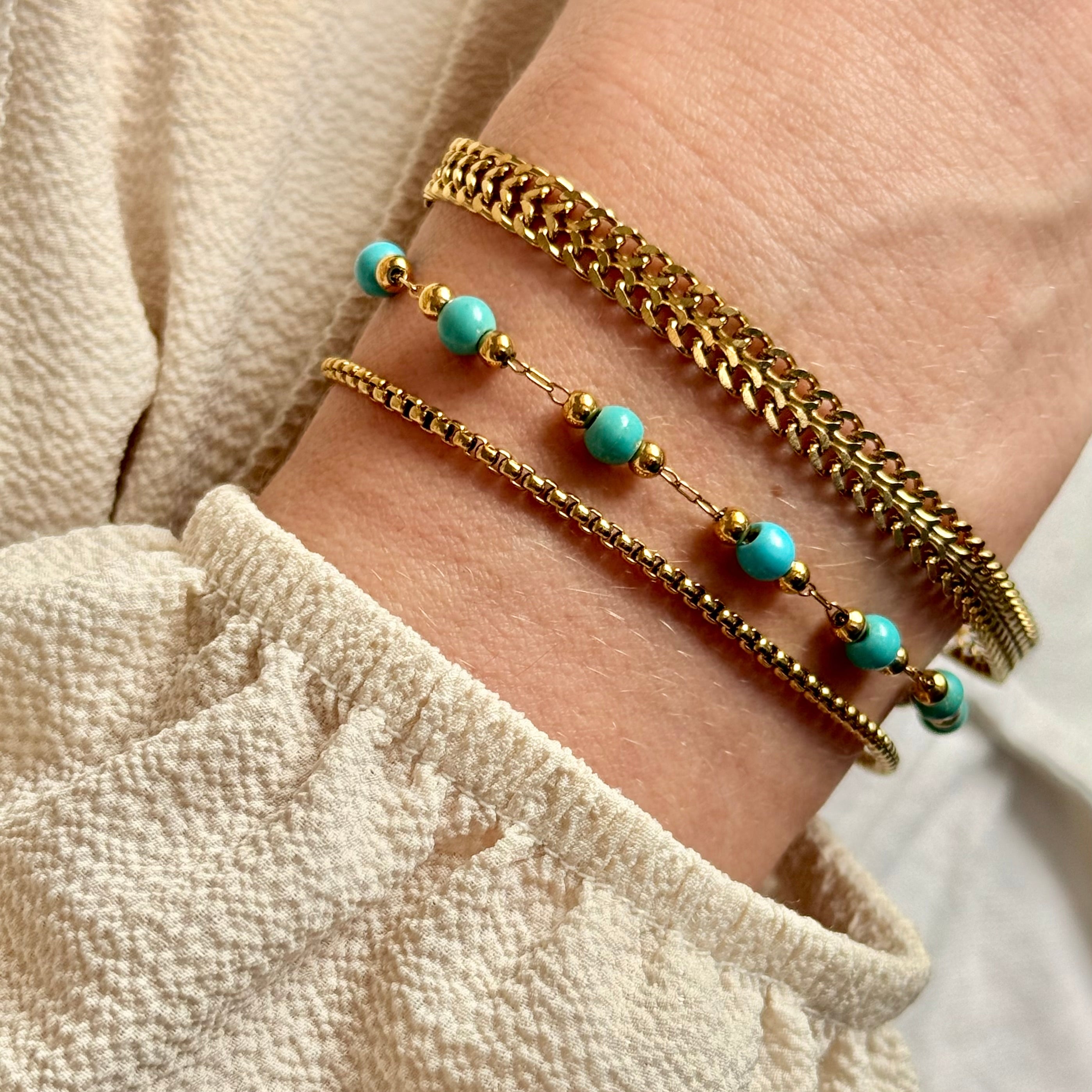 Close-up of a wrist wearing two gold bracelets with turquoise beads on a neutral background. braided gold bracelet, rope chain bracelet, dainty gold bracelet