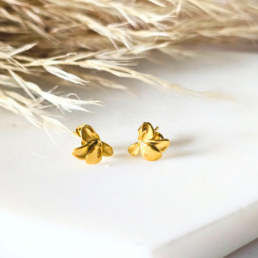 Gold flower earrings on a white surface with dried grass in the background