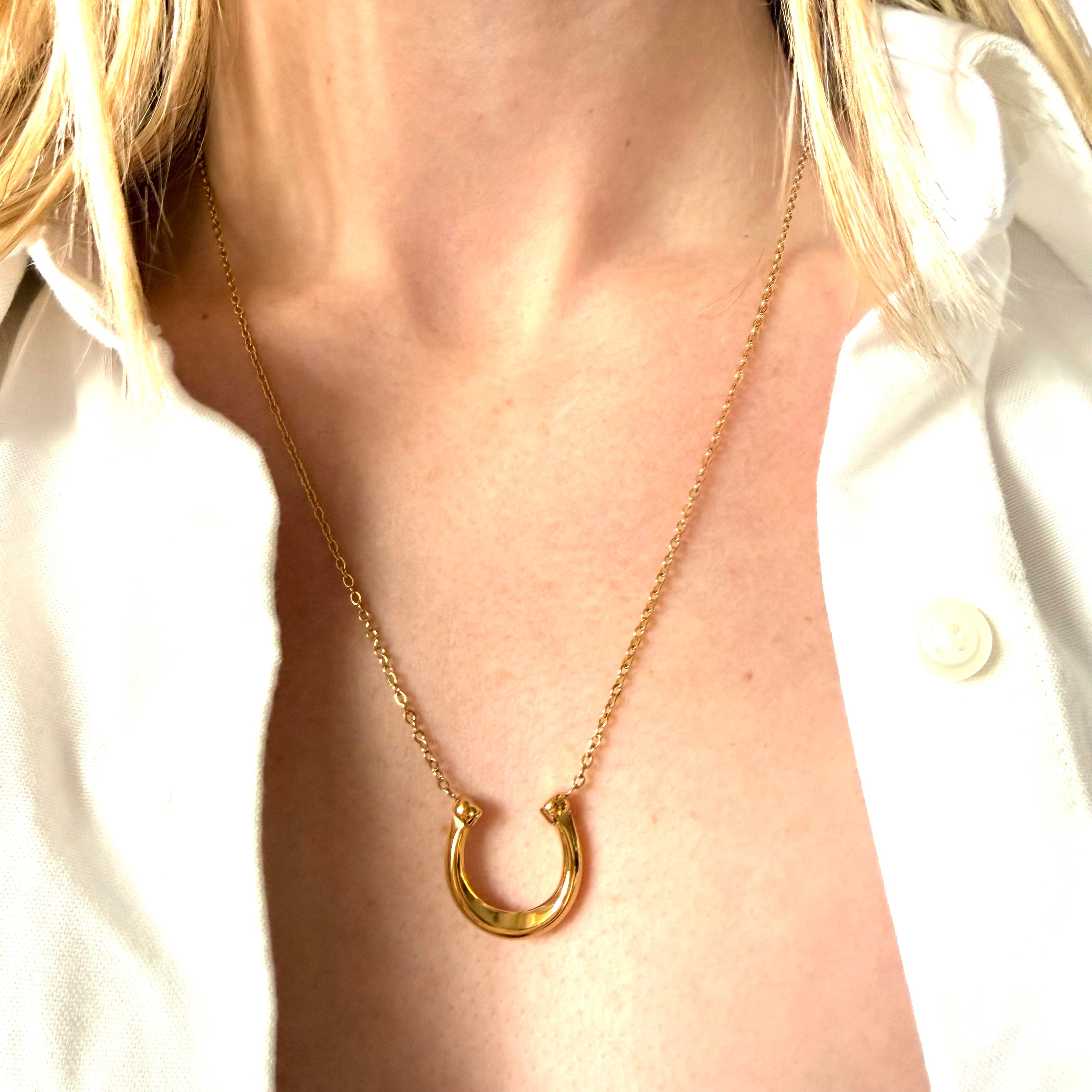Gold necklace with a horseshoe pendant worn by a person in a white shirt.