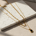 Gold chain necklace with a black pendant on a white background