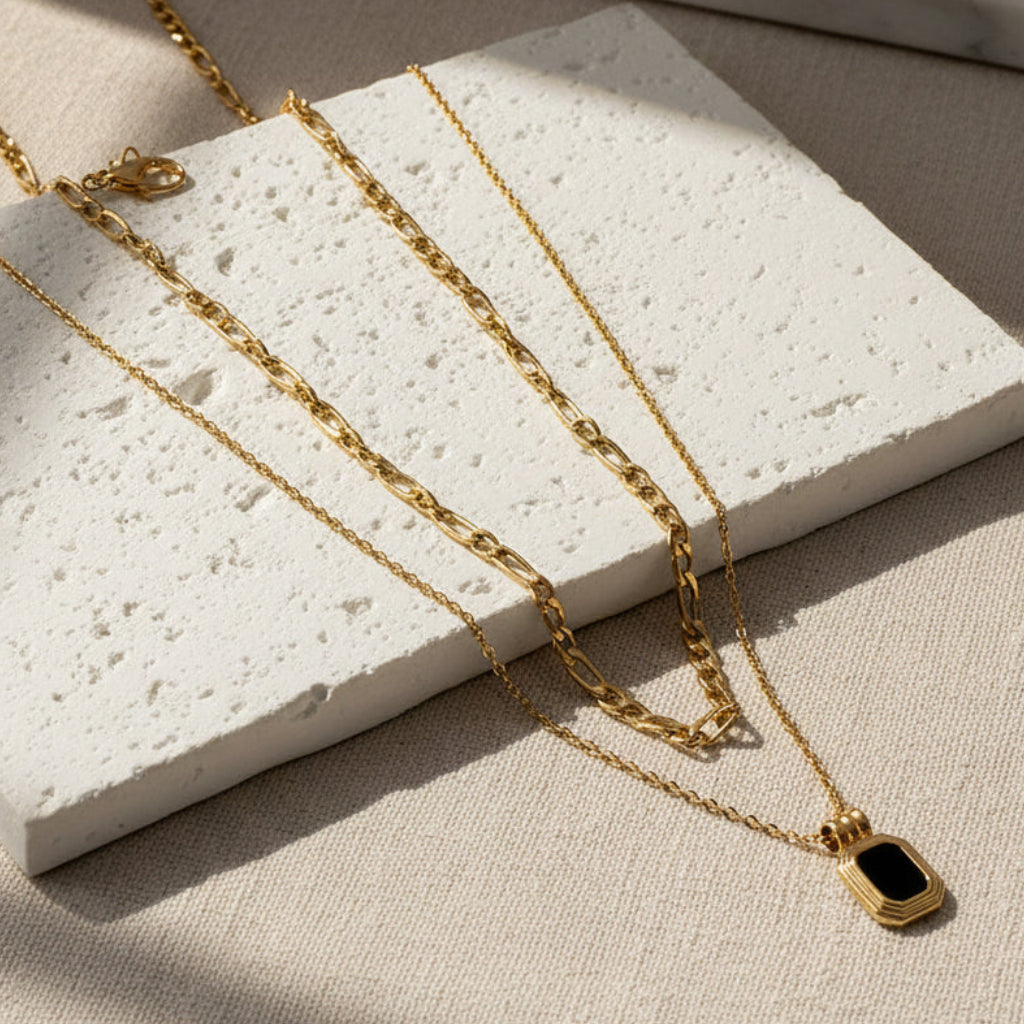 Gold chain necklace with a black pendant on a white background