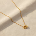 Gold necklace with two interlocked circle pendants on a marble surface