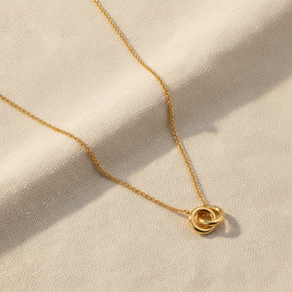 Gold necklace with two interlocked circle pendants on a marble surface